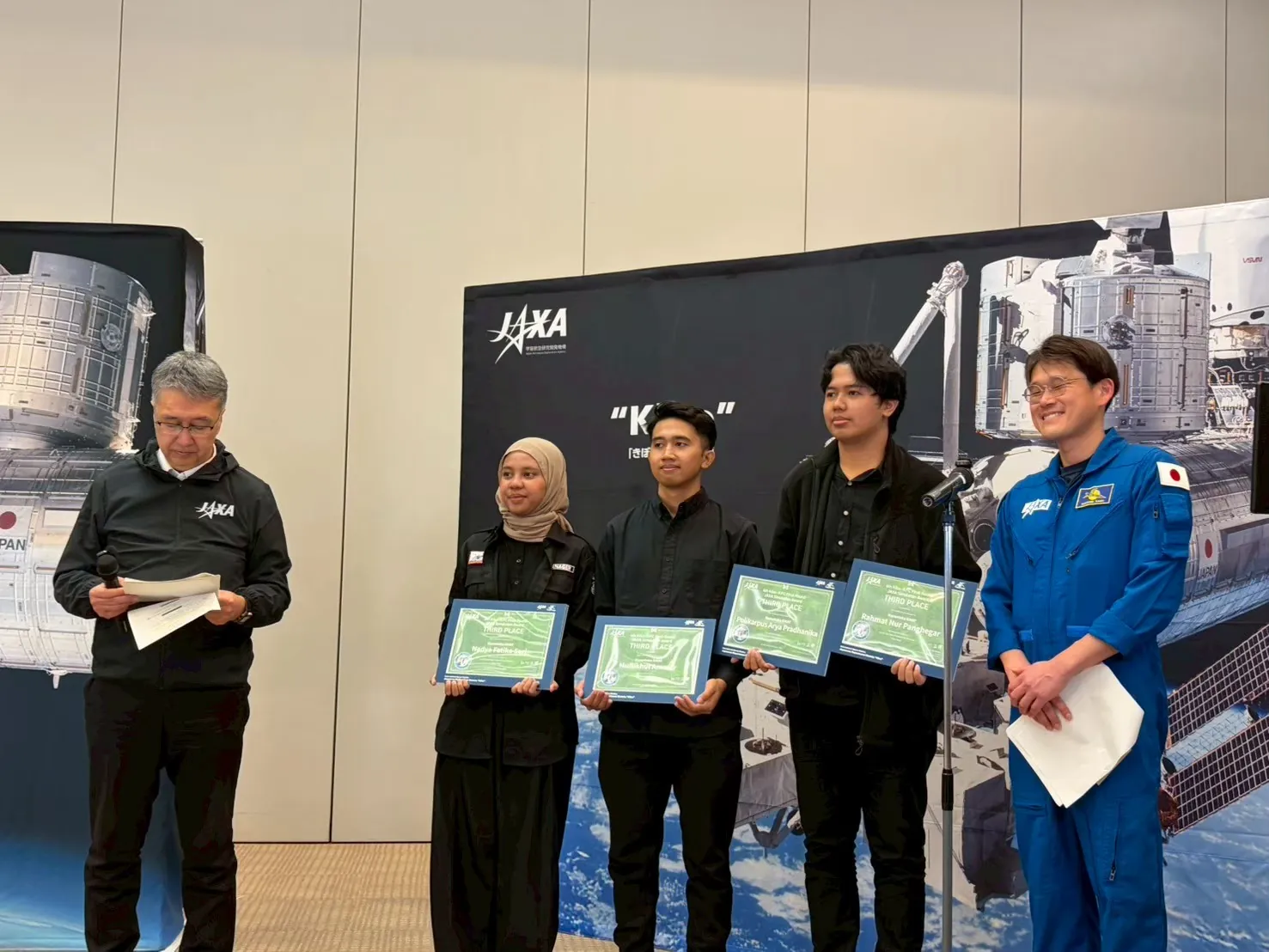 Tiga anggota tim memegang sertifikat di samping pejabat dan astronaut JAXA